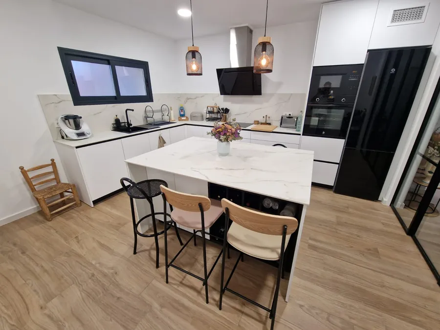 Cocina blanca con isla de porcelánico y frigorífico negro