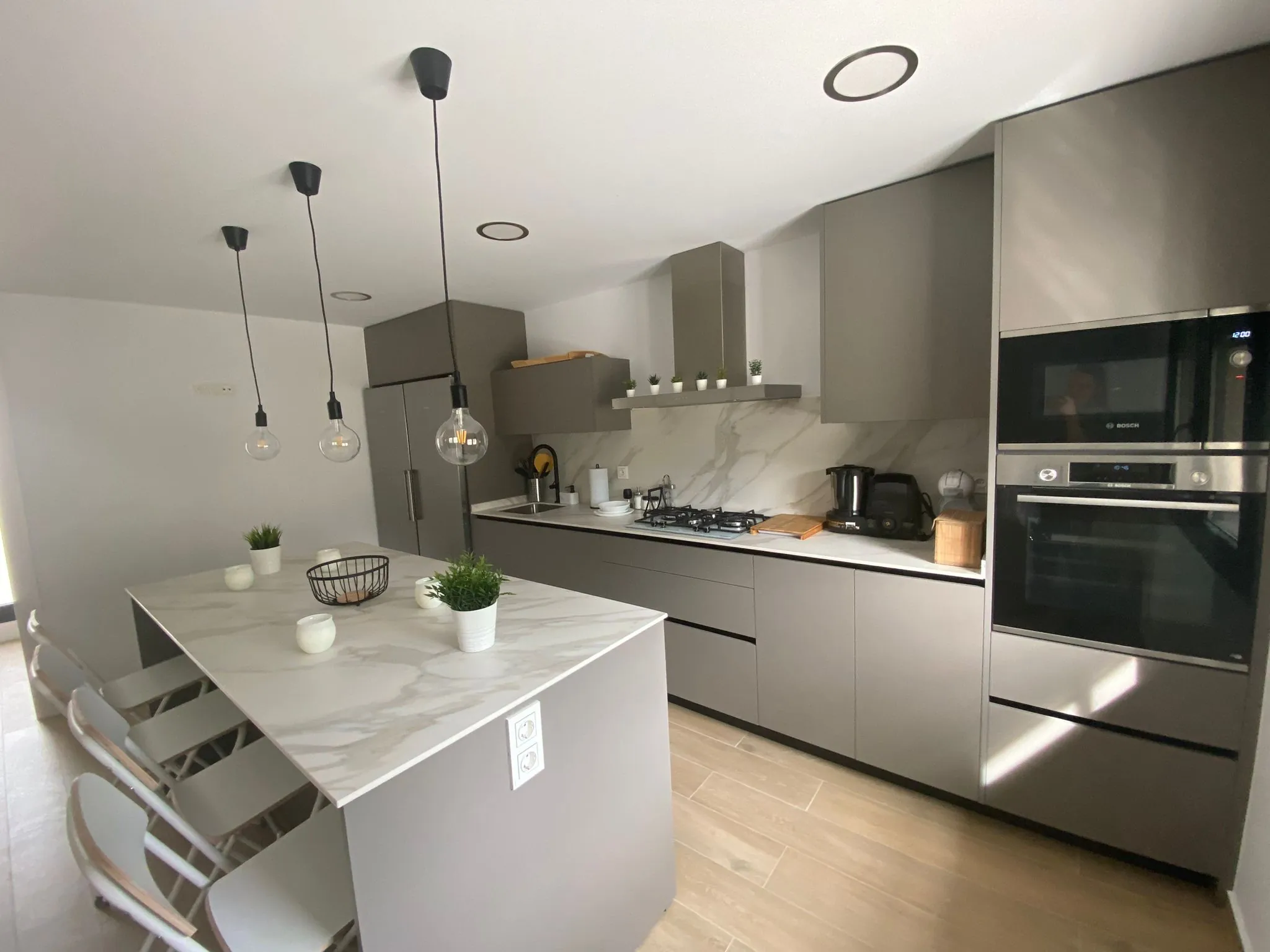 Cocina gris topo con isla de porcelánico blanco y columnas de horno